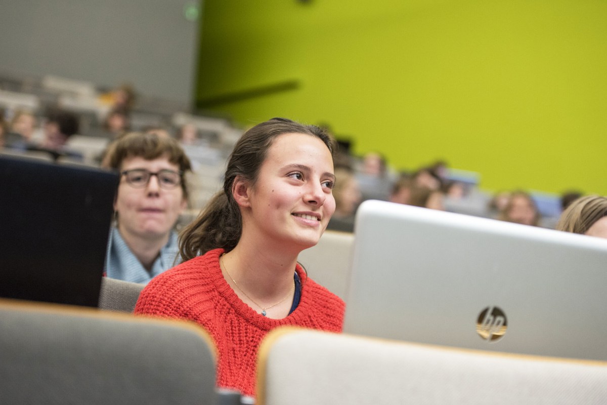Students listening in a bright lecture hall with soft green walls.