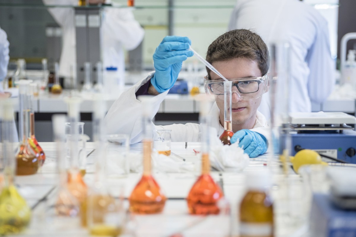 A researcher working carefully with glassware at a bright laboratory bench.