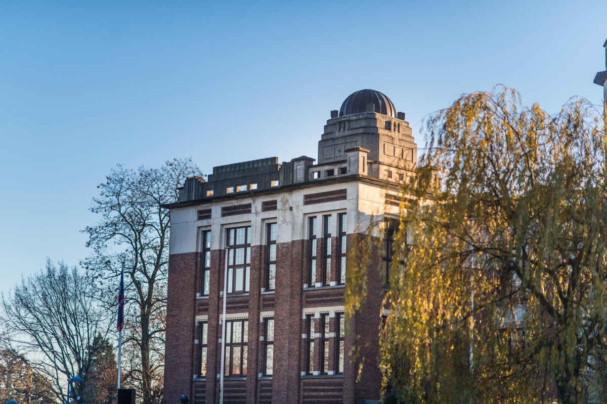 A historic brick building framed by tall trees and autumn foliage.