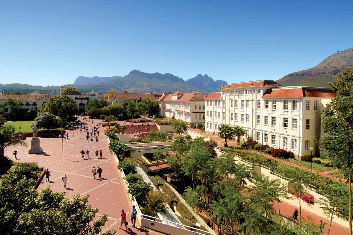A broad courtyard framed by campus buildings with mountains under a clear blue sky.