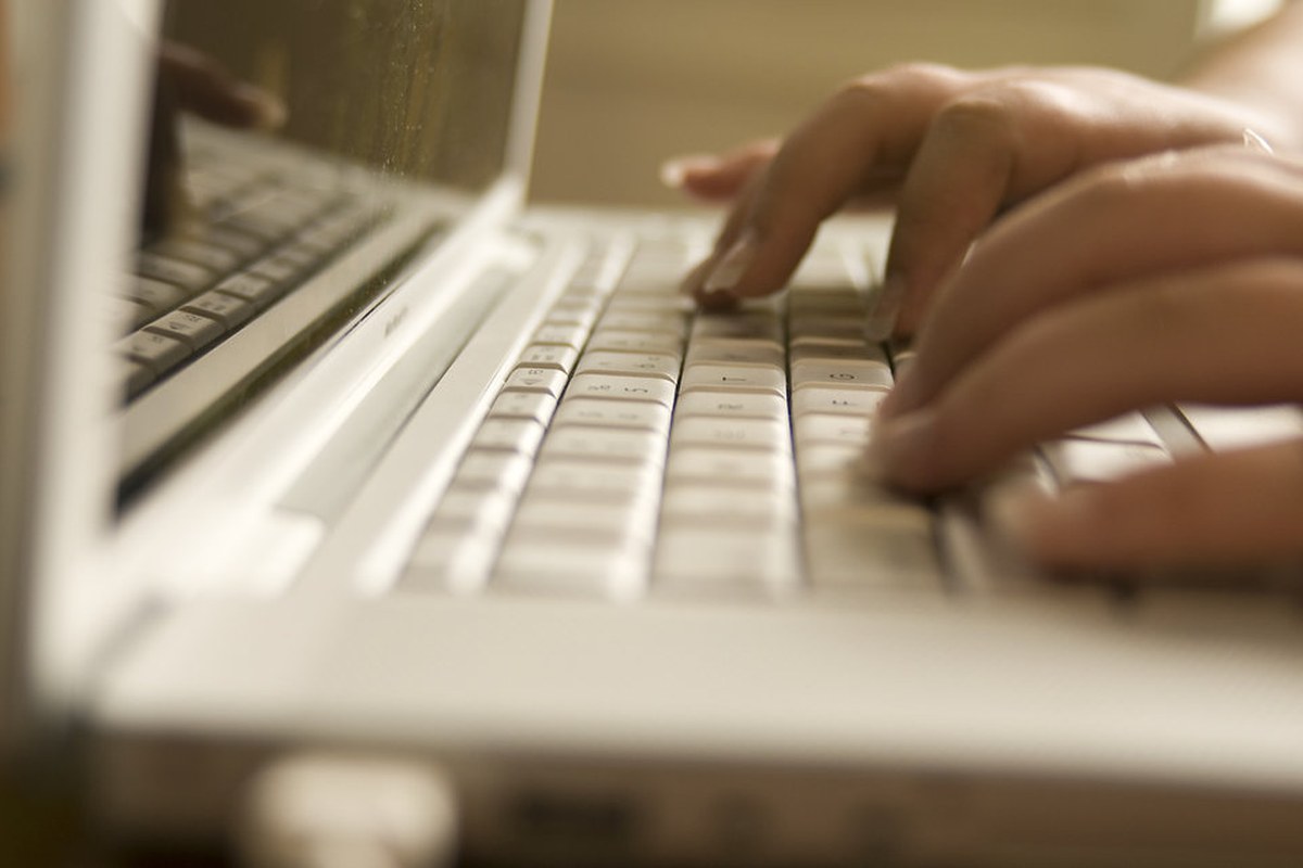 Hands typing on a laptop keyboard in warm indoor light.