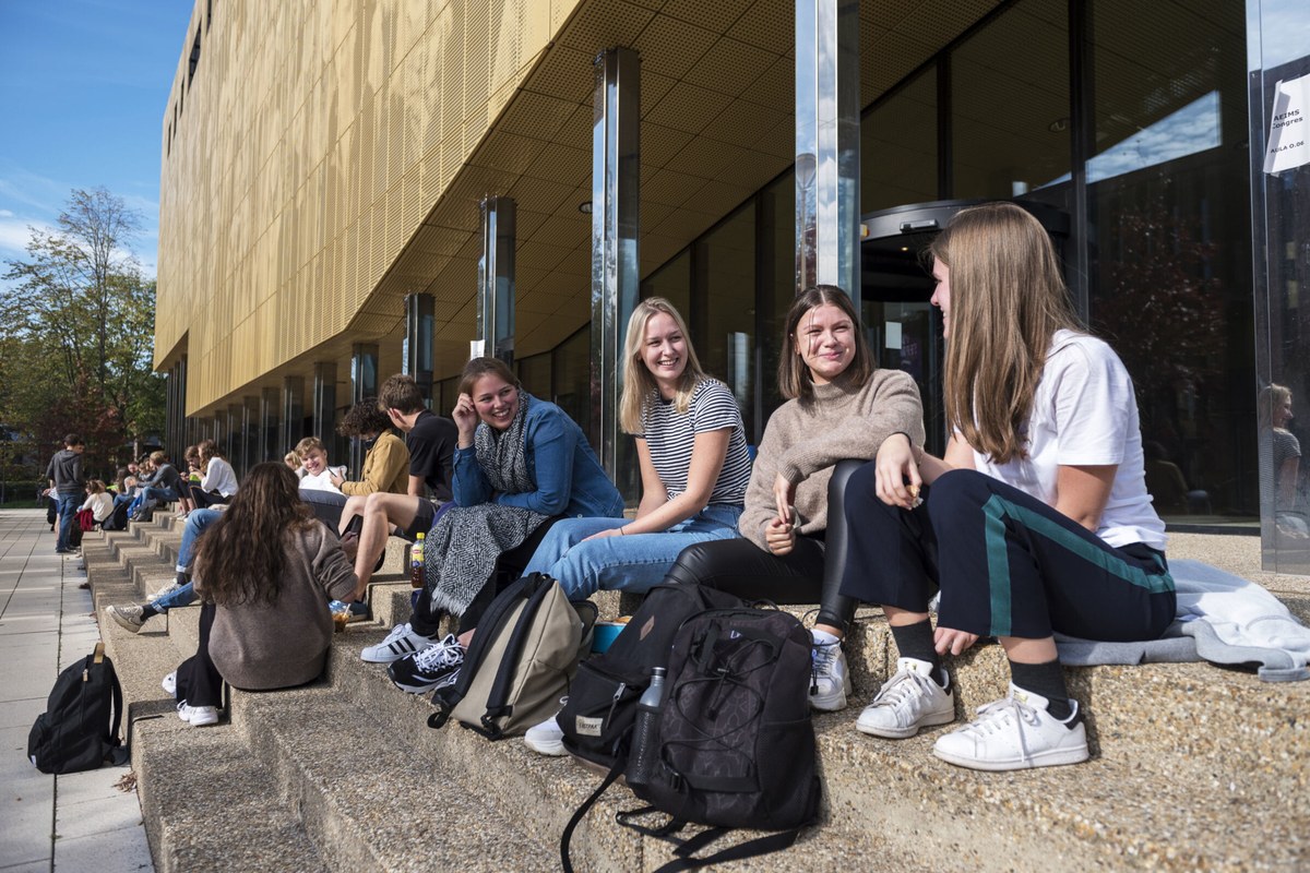 A small group of people sitting and talking outdoors beside a modern building.